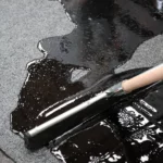 Iemand die met een rakel vloeibare waterdichting op roofing met leislag plaat voor renovatie en bescherming. Van het merk Schütz.